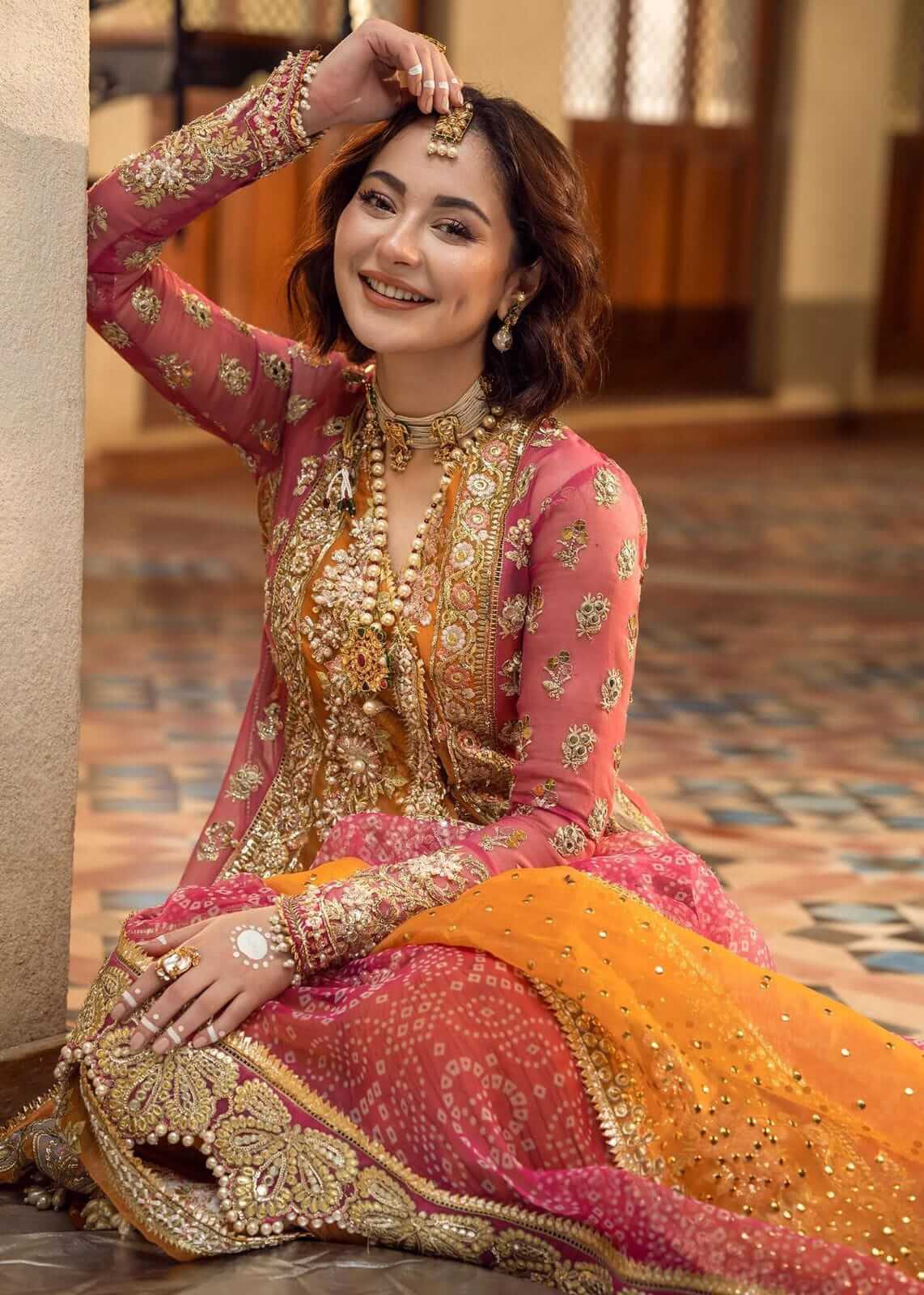 Woman in traditional pink and gold embroidered outfit sitting on a patterned floor.